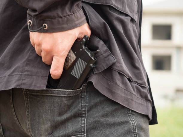 a man, policeman or robber, gangster concealing his gun behind his back - police crime gun gang member imagens e fotografias de stock