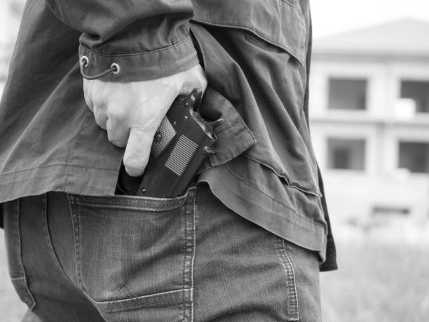 un homme, un policier ou un voleur, un gangster cachant son arme dans son dos - police crime gun gang member photos et images de collection