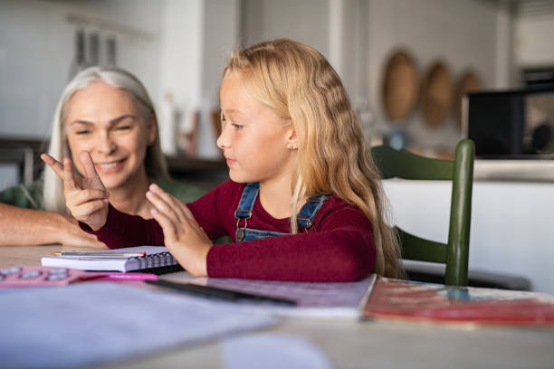 Child counting addition and subtraction on fingers while doing math homework. Elementary student with grandmother solving multiplication table in notebook and counting on fingers. Granny helping granddaughter in mathematics sum at home.