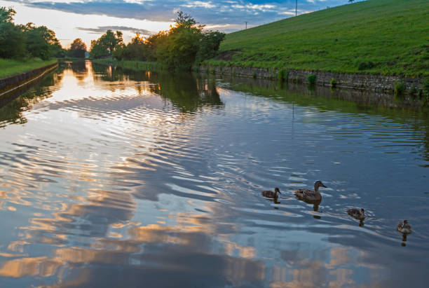 View of an English rural countryside scenery on British waterway canal during overcast cloudy day at sunset dusk
