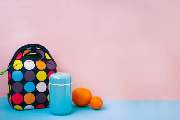snack on a break with a lunchbox. colorful handbag, blue thermos, orange, tangerine. place for text, pink background. snack on a break with a lunchbox. colorful handbag, blue thermos, orange, tangerine. place for text, pink background packed lunch photos stock pictures, royalty-free photos & images