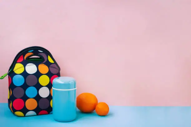 snack on a break with a lunchbox. colorful handbag, blue thermos, orange, tangerine. place for text, pink background