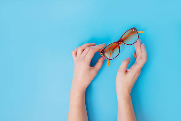 Female hands holding glasses on blue background.