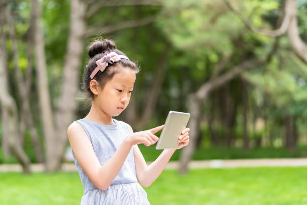 istock A cute asian little girl using digital tablet in public park 1161415712