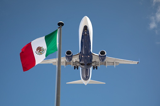 Bottom View of Passenger Airplane Flying Over Waving Mexico Flag On Pole.