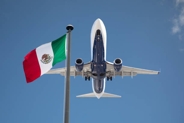 Bottom View of Passenger Airplane Flying Over Waving Mexico Flag On Pole stock photo