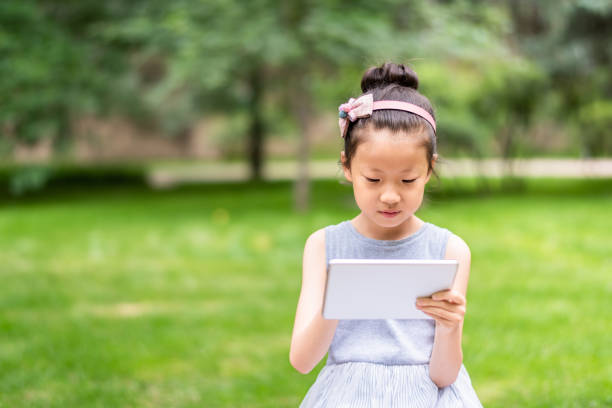 istock A cute asian little girl using digital tablet in public park 1161416347