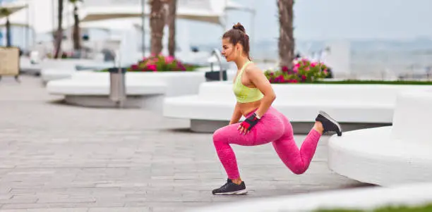 Young attractive woman doing lunges with one leg exercise outdoors in urban environment