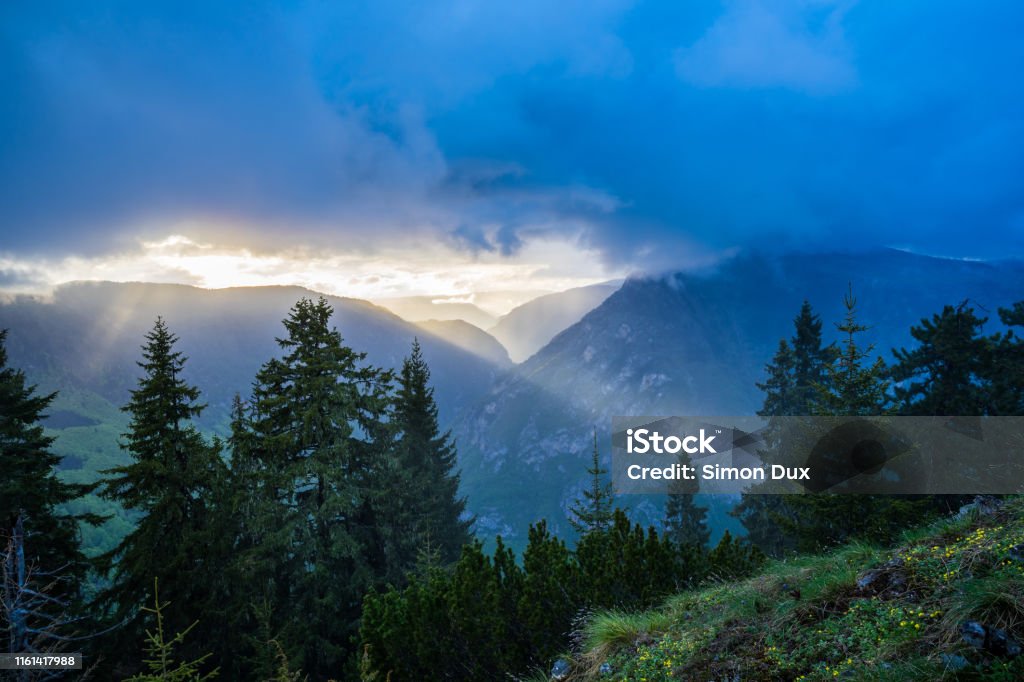 Montenegro, Warm orange sunset light breaking through clouds over tara river canyon from peak viewpoint of mount curevac in durmitor national park Atmospheric Mood Stock Photo