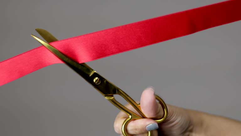 A woman hand with gold scissors cutting red ribbon