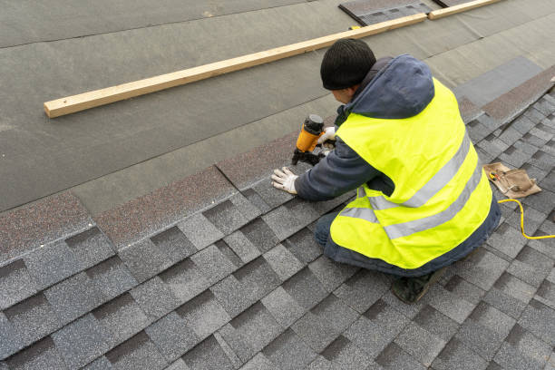 qualifizierter arbeiter in gleichmäßiger arbeitskleidung mit luft- oder pneumatik-nagelpistole und montage von asphalt- oder bitumenschindeln auf dem neuen dach im bau wohnhaus - dachdecker bauarbeiter stock-fotos und bilder