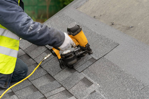 istock Close up and real photo of unrecognizable workman in protective uniform using air or pneumatic nail gun and installing asphalt or bitumen tile on top of the roof under construction house 1161429590