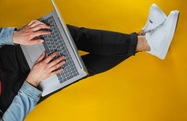 istock Online worker concept. Hipster man typing on laptop and sits on yellow background. Studio shot. Top view 1161429667