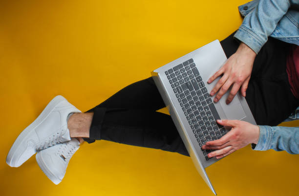 istock Online worker concept. Hipster man typing on laptop and sits on yellow background. Studio shot. Top view 1161429709