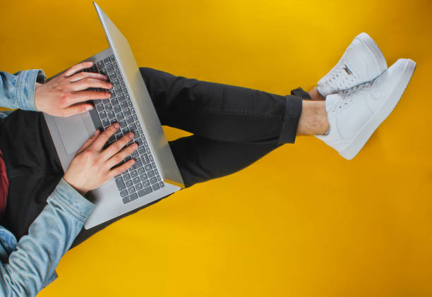 istock Online worker concept. Hipster man typing on laptop and sits on yellow background. Studio shot. Top view 1161429712