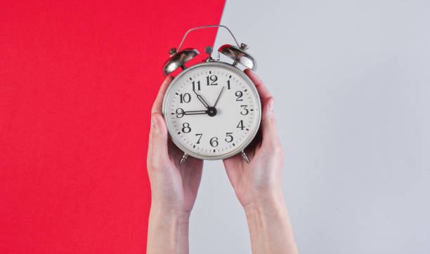 istock Female hands hold retro alarm clock on red gray background 1161429738
