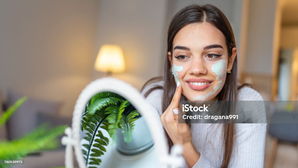 Natural homemade facial masks at home. Natural homemade facial masks at home. Woman applying mask on her face and looking in the mirror. Beautiful woman applying natural facial mask. Beauty treatments. Skin Care Stock Photo