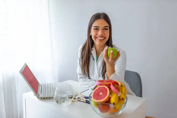 Nutritionist desk with healthy fruits, juice and measuring tape. Dietitian working on diet plan at office, smiling at camera. Weight loss and right nutrition concept.