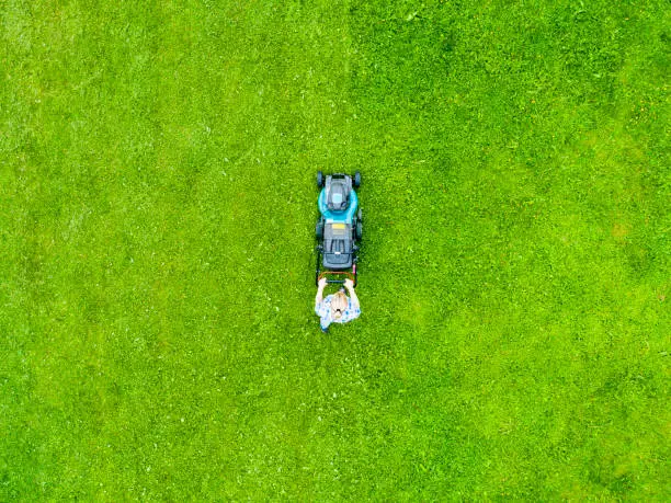 Photo of Beautiful girl cuts the lawn. Mowing lawns. Aerial view beautiful woman lawn mower on green grass. Mower grass equipment. Mowing gardener care work tool. Close up view. Aerial lawn mowing