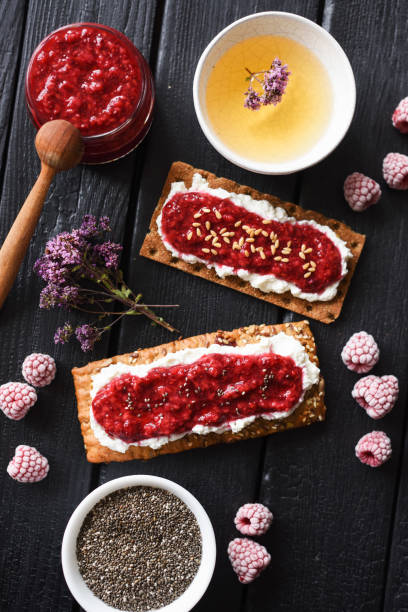 istock Healthy sugar free dessert and herbal tea. Raspberry chia jam on crispy bread and cream cheese with frozen berries on black background 1161440465