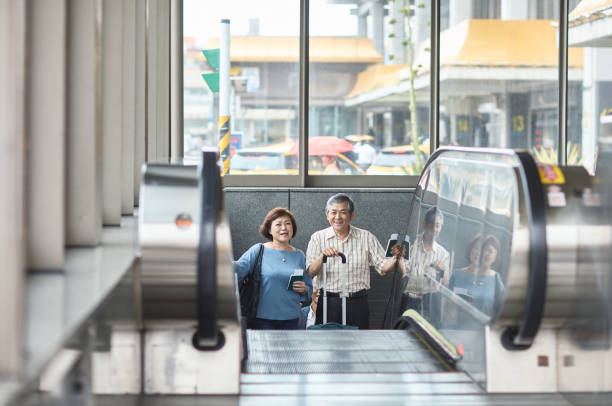 공항에서 에스컬레이터를 타고 웃고 있는 시니어 아시아 여행객 - senior adult close to moving up togetherness 뉴스 사진 이미지