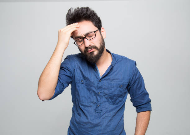 portrait of frustrated young man over grey background - head in hands imagens e fotografias de stock