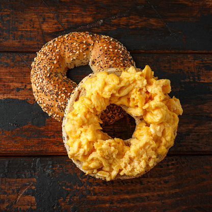 Bagels breakfast sandwich with scrambled eggs on wooden table.