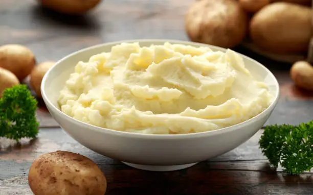 Photo of Mashed potatoes in white bowl on wooden rustic table. Healthy food