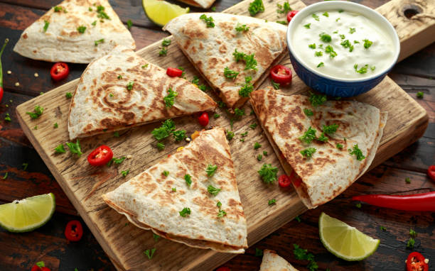 istock Mexican quesadilla with chicken, corn, black beans, cheese, vegetables, lime and yogurt sauce on wooden board 1161444301
