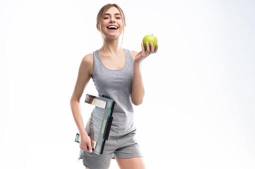 Healthy woman stands with the scales and green apple. Healthy eating concept