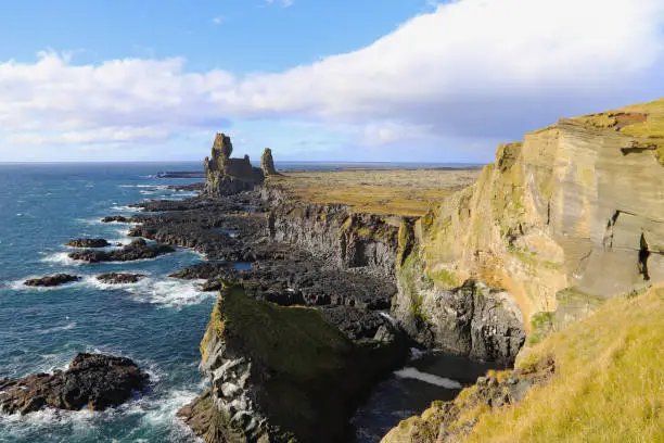 Photo of Rock and lava formations along the coastline and the Londrangar basalt cliffs on the southern coast of Snaefellsnes peninsula in West Iceland. The Londrangar basalt cliffs - huge towers of lava.