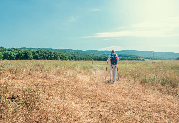 Happy girl in white with a backpack and walking stick set in nature