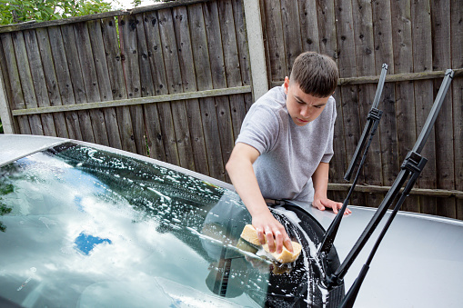 Teenage boy washing a car windscreen on a warm summer's day