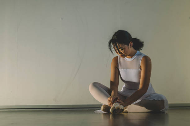 un'adolescente cinese asiatica si è ferita una gamba durante l'allenamento nel suo studio di balletto e si è seduta sul pavimento con dolore - scuola di danza classica foto e immagini stock