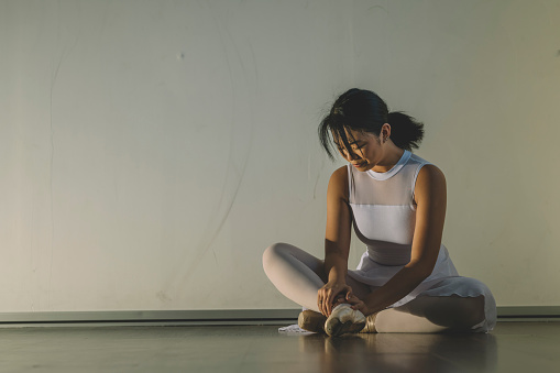 an asian chinese female teenager hurt her leg during practise in her ballet studio and sit on the floor with pain