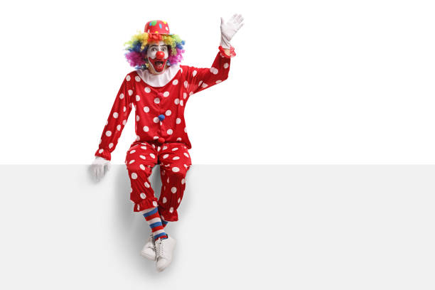 istock Funny clown sitting on a white panel and waving 1161459848