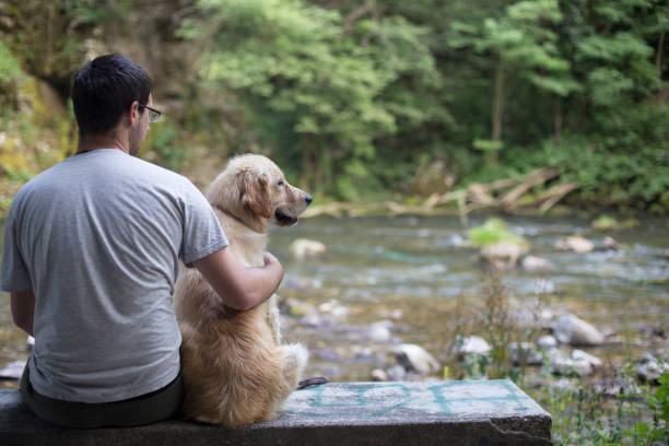 Young man sitting with his dog on the chair in the park, enjoyin.