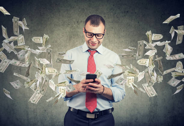istock Happy business man using smartphone with dollar bills flying away from screen 1161469428