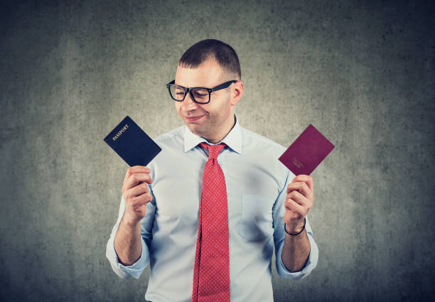 A man in a shirt and tie holds two different passports and compares them with a thoughtful expression.