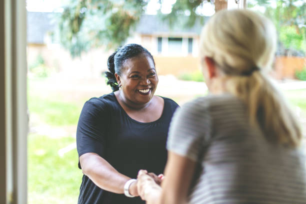 adult african american female e caucasica davanti alla porta di residenza salutarsi con una stretta di mano - vicino di casa foto e immagini stock