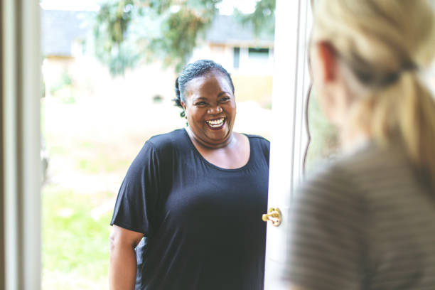 erwachsene afroamerikanische frau und kaukasier vor der haustür der residenz grüßen einander - neighbors at the front door stock-fotos und bilder