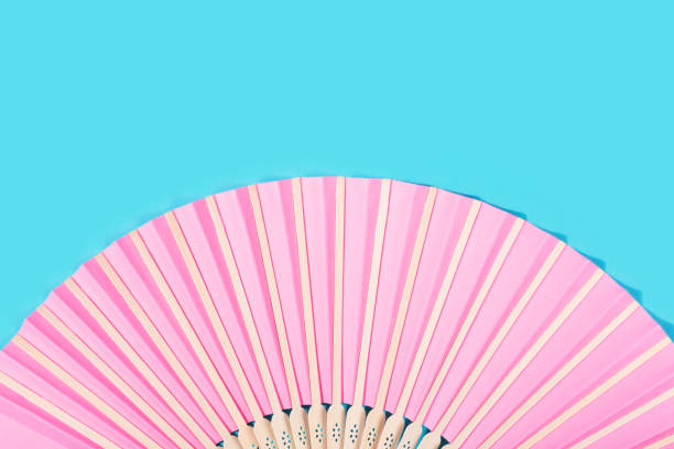 Beautiful pink fan on turquoise background. Summer concept. Elegant refreshment. Copy space.