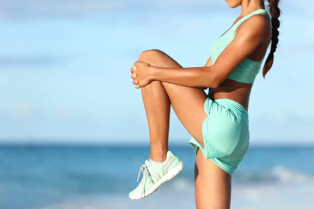 Photo of Runner stretching leg during outdoor warm-up on beach before run