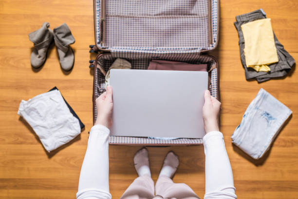 vista dall'alto delle mani delle donne che impacchettano il laptop nel bagaglio (valigia) per un nuovo viaggio. - skirt women jeans white foto e immagini stock