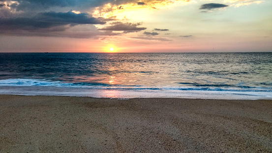 Sunset over the ocean from the shore of Nazaré beach, Playa do Norte, Portugal. The waves break on the shore reflecting the colors of the sky on the wet sand