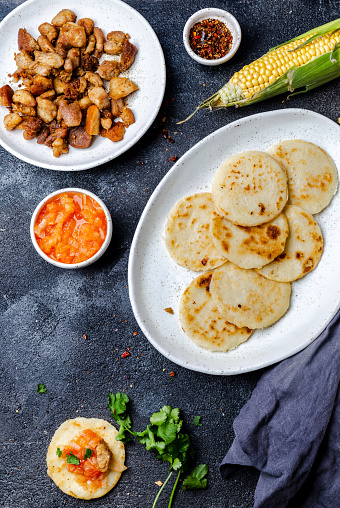 COLOMBIAN FOOD. Maize AREPAS and fried pork chicharron ans colombian tomato sauce. Top view. Black background.