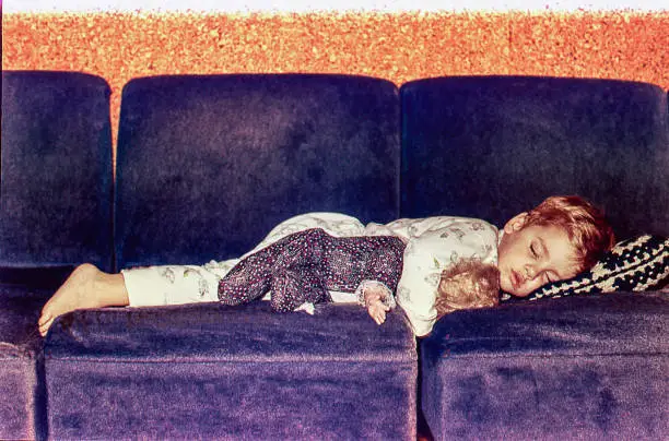 Vintage image of a cute kid sleeping on a sofa with her doll.