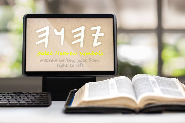 A tablet showing the paleo Hebrew symbols for the name of God on a desk with a keyboard, opened holy bible and cross in background. stock photo