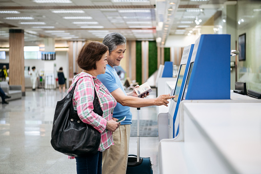 Active senior Chinese couple using touch screen display to confirm identity in airport terminal, travel, technology, retirement