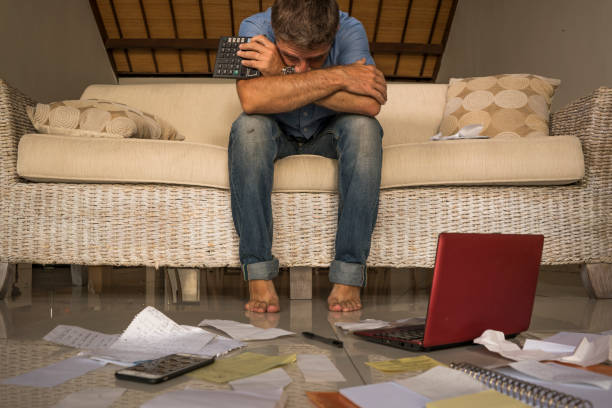 young attractive stressed and frustrated man at home living room couch doing domestic accounting overwhelmed and worried suffering financial problem going over taxes and payments paperwork stock photo